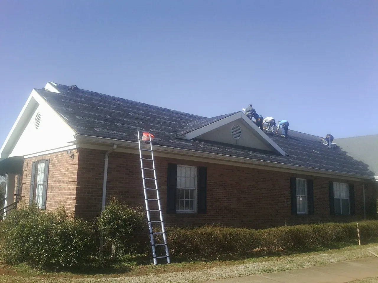 Crew tearing shingles off a brick ranch roof with a ladder set — Metal Roof Repair work by our crew in Lafayette