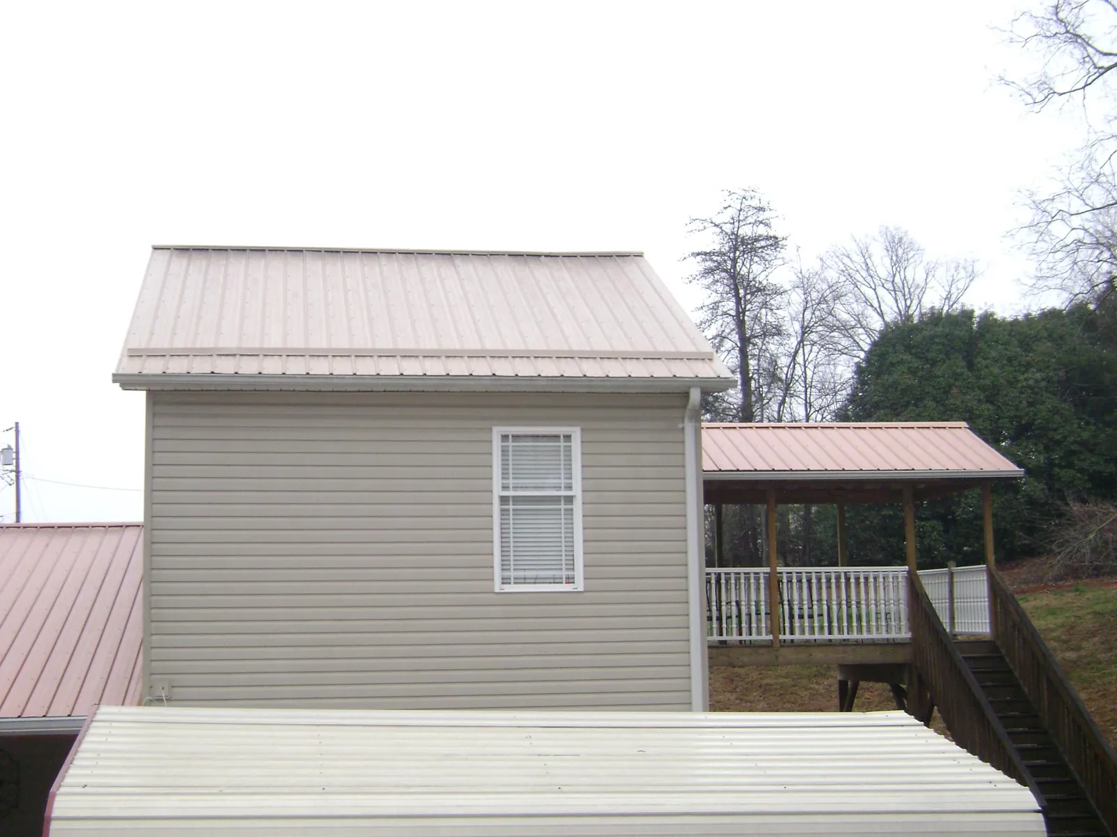 Tan metal roofs on a two story addition and attached porch, from a Roof Replacement job in Lafayette